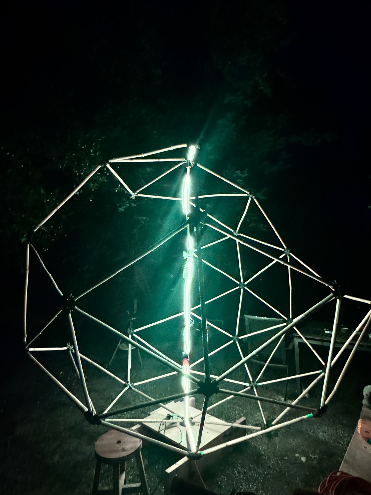 The bamboo geodesic frame assembled in a garden in daylight — a full sphere of struts and black hub connectors on a timber base, a stepladder alongside.