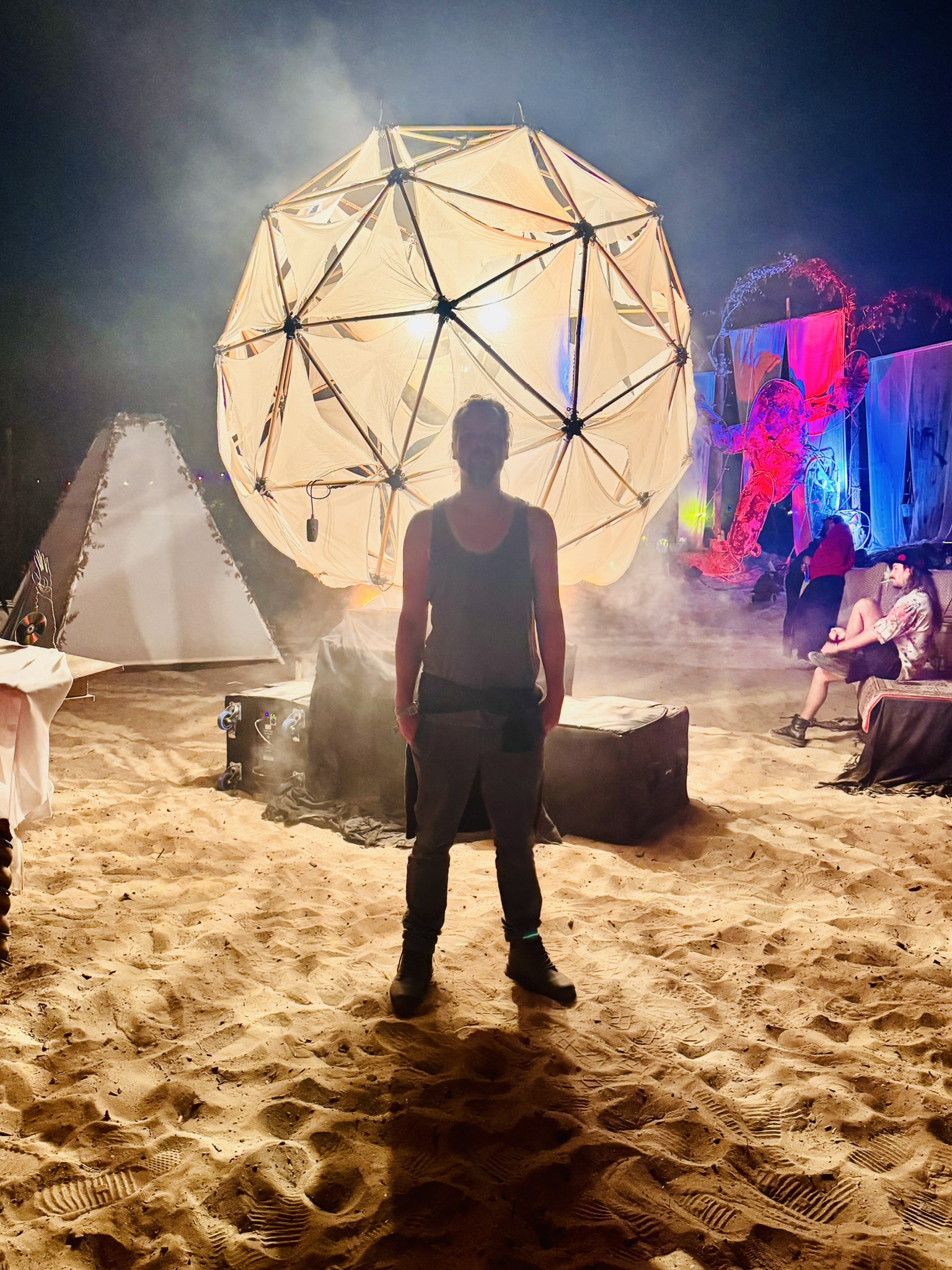 Jasper Veldkamp standing on the sand in front of Sól, silhouetted against the glowing geodesic orb at night.